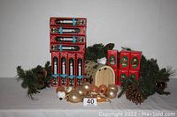 Photo showing the entire lot including stacked boxed holiday lights, porcelain Santa figurine boxes, green garland, decorative balls, pine cones, and wooden Santa mailbox.