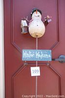 Close-up front view of the snowman figure holding birdhouse and lantern with Winter Welcome sign beneath it on metal pole.