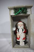 Frontal close-up of Santa figurine inside outhouse showing detail of Santa holding list