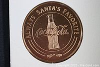 Close-up of bronze medallion showing Coca-Cola bottle and 'Always Santa's Favorite' inscription