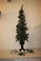 Full view of the tall thin artificial accent tree with pine cone decorations and dark urn-shaped base, standing almost 6 feet tall.