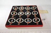 Complete set of 12 Thomas Pacconi Christmas ornaments displayed in original red box with black velvet interior, arranged in 3 rows of 4.