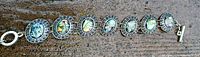 Full view of the abalone shell bracelet showing all oval stones and silver-tone frames on a textured surface.