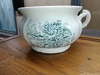 Side view of white semi-vitreous chamber pot with green chrysanthemum transferware decoration and applied handle