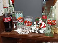 Full lot arranged on shelf showing two Coca-Cola glass bottles, two branded drinking glasses, and three polar bear Coca-Cola figurines next to a miniature jukebox