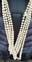 Front view of four strands of white faux pearl beads arranged against a dark background showing uniform bead size and lustrous finish.