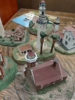 Photo showing three Danbury Mint lighthouse miniatures with detailed bases and trees, plus a portion of the Old Point Loma lighthouse booklet visible on table.