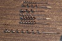 Eight extra large drill bits laid out on carpet, showing length and width differences.