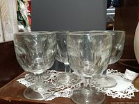 Five heavy glass goblets grouped together on a lace mat.