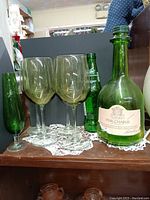 Photo showing four green-tinted tall wine goblets, a vintage Gallo Pink Chablis green wine bottle with label intact, a classic green Sprite bottle, and a vintage green bud vase. Items are placed on a lace doily.
