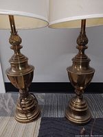 Pair of Mid-Century Modern brass table lamps with fabric shades. Lamps have a polished brass body with sculptural details and some staining visible on shades.