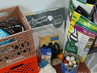 Overview photo showing two milk crates filled with electrical cords and small tools, an American Standard toilet seat box, a Flowmaster sprayer box, bucket of golf balls, white gloves, and assorted small tools in front.