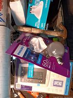 The lot of miscellaneous tools and household supplies including hammer, light bulbs, drywall tape, and electrical device, shown from one angle.