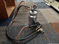 Full view of pressurized paint sprayer with attached hoses and brass fittings on floor.