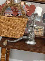Close-up of vintage metal hand-crank meat grinder with wooden handle next to woven basket