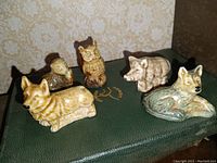 Five small Wade pottery animal figurines arranged on a dark green textured surface, showing owl, corgi, otter, boar, and wolf.