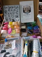 Photo showing multiple small packs of colorful wool roving, a hexagonal DIY wool felting guide pamphlet, black foam pad, decorative stencil sheet, and some felting tools.
