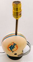 Front side view of vintage 1973 Miami Dolphins helmet lamp with logo and stripes visible, on black base, lamp socket without bulb visible on top.