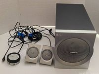 Overall lot showing subwoofer, two satellite speakers, control pod, and cables on a plain background