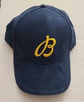 Front view of deep blue fabric hat with yellow embroidered "B" logo on the crown.