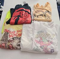 Seven folded graphic t-shirts stacked in two rows showing designs and logos representing vintage and club themes.