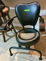 Front view of black Dr Son Hula Chair Massager with padded seat, backrest, and armrests on a tiled floor.