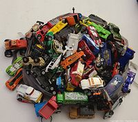 Overhead photo of a large pile of toy cars including sports cars, trucks, and specialty vehicles in multiple colors and conditions.