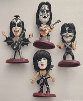 Front view of four KISS headliner figures showing each band member with detailed stage makeup and outfits, standing on red bases with names.