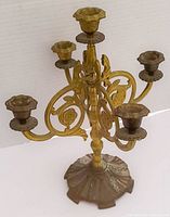 Front angled view of vintage brass 5-arm candelabra showing decorative floral scrollwork and patina.