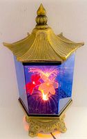 View of lantern showing color changing fiber optic flower lit in red and yellow hues, pagoda-style gold roof and ornate base.