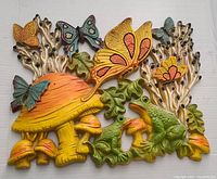 Front view of the colorful wall hanger showing mushrooms, butterflies, green leaves, and a frog figure.