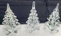 Three clear glass art Christmas trees with varied branch shapes against a dark background