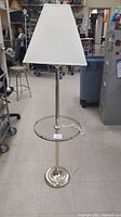 Full view of the brass floor lamp with white fabric lampshade and attached glass table, showing entire height and base.