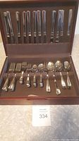 Full view of the Lagostina silverware set inside a wooden storage box showing knives secured in the lid and assorted forks, spoons, and other utensils organized below.