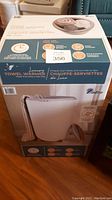 Towel warmer in original box showing brand and product features including timer and fabric compatibility.
