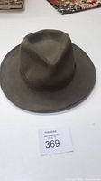 Brown wool felt fedora style hat with wide brim and tapered crown on white surface.