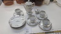 Complete tea set with tea pot, cream pitcher, sugar bowl, 4 tea cups with saucers, and 4 side plates arranged on a table.