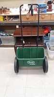 Front view of green Scotts AccuGreen garden spreader showing green plastic container, black handle and two wheels.