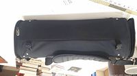 Side view of black cylindrical luggage bag with attached padded shoulder strap on table.