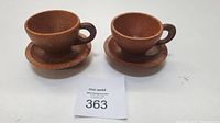 Two wooden tea cups displayed on separate matching wooden saucers on white surface.