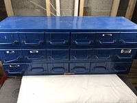 Front view of the blue steel cabinet showing all 18 drawers with metal handles and label slots. Surface shows light scratches and wear.