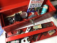 Open red metal toolbox showing internal bicycle tools, repair manual, and parts.