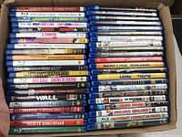 Photo showing the full view of Blu-ray and DVD movie cases stacked tightly in a box, titles listed clearly on spines.