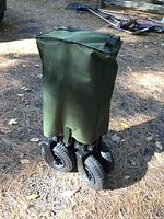 Folded cart showing green canvas cover and black wheels on natural ground.