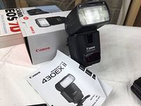 Canon 430EX II Speedlite flash on its box with instruction manual and two books around it.