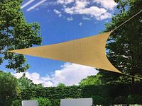 Coolaroo tan triangle shade sail tightly stretched outdoors between trees under a sunny blue sky with clouds.