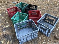 Seven plastic crates of various colors arranged outside on pine straw and leaves.