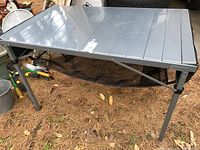 Full view of the aluminum camping table set up on outdoors ground showing its legs and size.