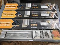 Four boxes of Alu-rex Clip ’n’ Guard Rain Gutter Protection guards stacked showing packaging branding; one package open showing perforated aluminum panels.