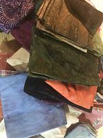 Pile of assorted fabrics in various solid colors and tie-dye style patterns including blue, orange, black, green, and purple